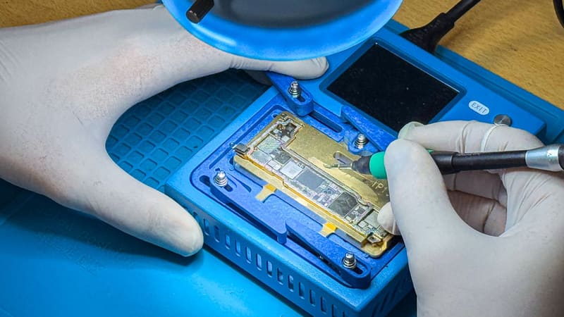 Een iPhone-moederbord in een houder wordt met een fijne soldeerbout bewerkt