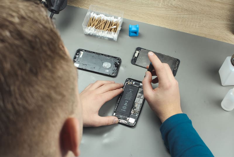 Twee handen werken aan een geopende iPhone tussen losse onderdelen op de werkbank