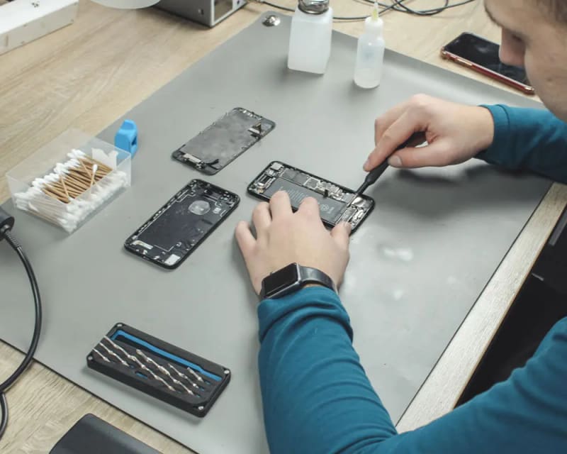 Drie geopende iPhones op een grijze werkmat, met gereedschap en wattenstaafjes