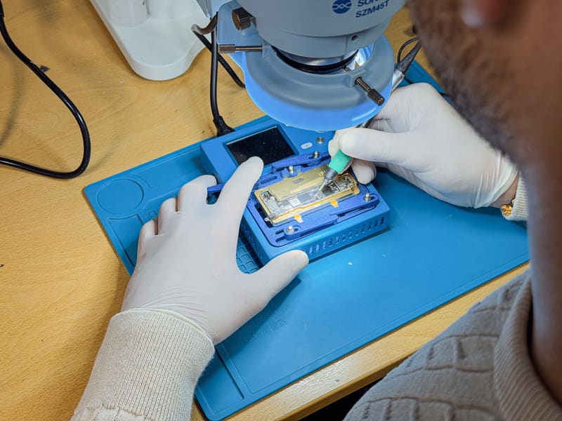 Microsolderen onder de microscoop: een moederbord in de houder op een blauwe werkmat