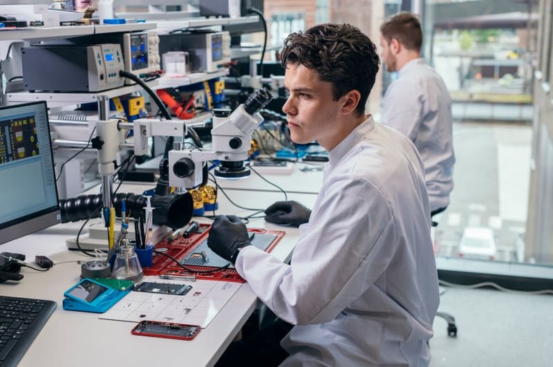 Cursist aan een werkplek met microscopen en soldeerapparatuur