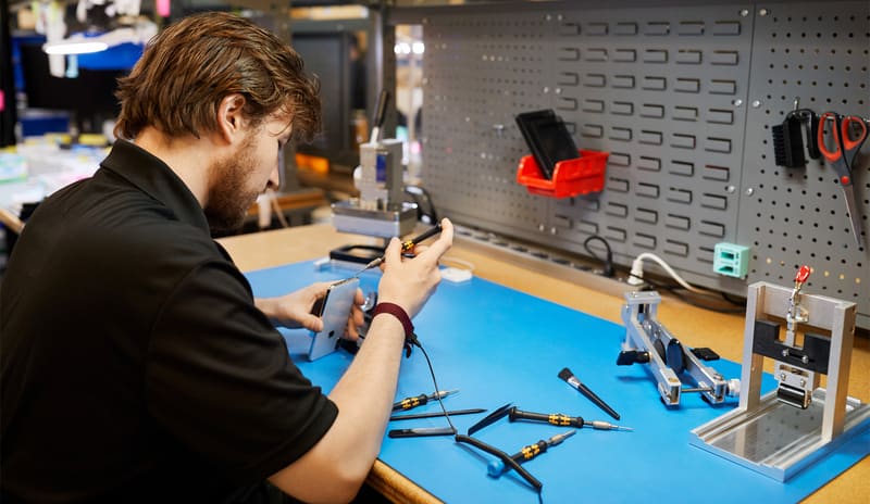 Reparateur aan de werkbank met schroevendraaiers en een smartphone